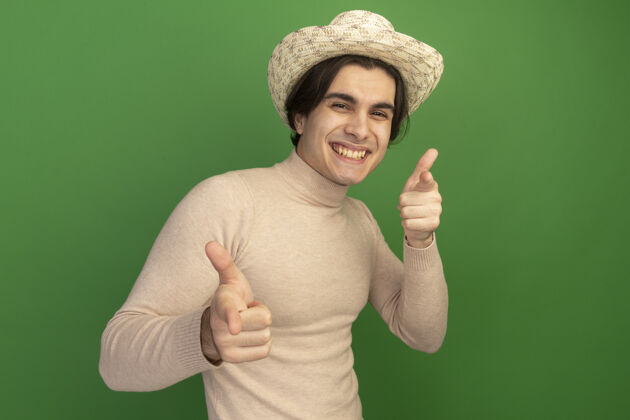 手势带着微笑的年轻帅哥戴着帽子 在绿色的墙上展示着你孤立的姿态男人微笑帽子