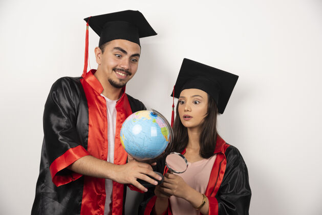 男人穿着长袍的应届毕业生看着白色的地球仪女人站着帽子