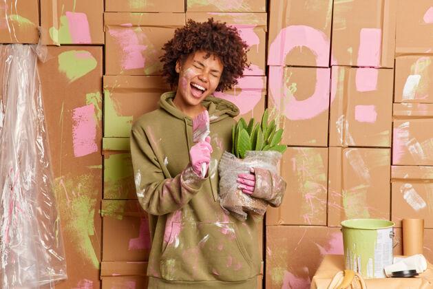 工作快乐的黑皮肤年轻女子在公寓里修缮油漆墙后在画笔里唱歌欢乐肮脏刷子