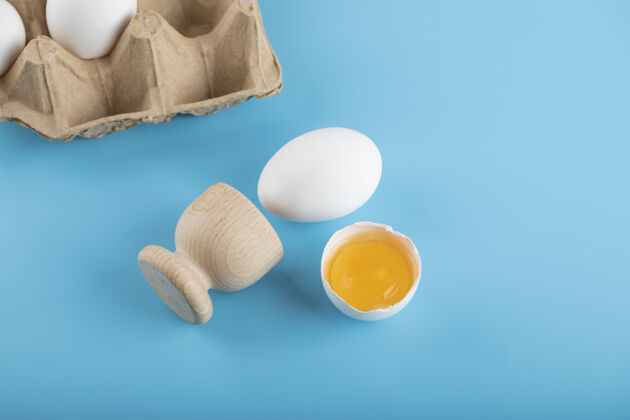 蛋黄破碎的生鸡蛋和蓝色表面的鸡蛋容器生的鸡蛋烹饪