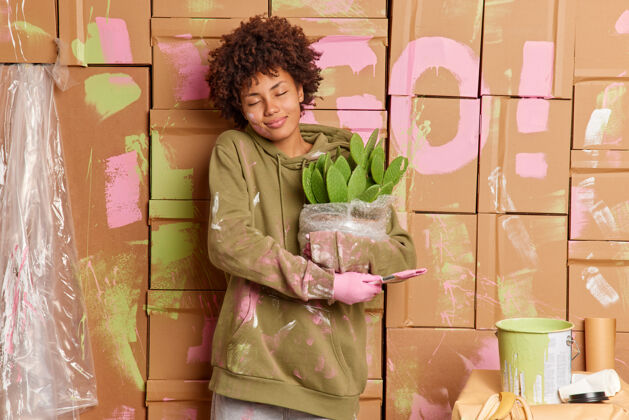 涂抹高兴的年轻非洲裔美国妇女享受装修时间在家里涂上油漆举行刷盆栽仙人掌重新安置在新的公寓室内工作女性