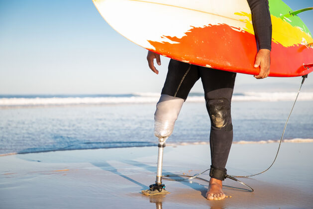 板无法辨认的男性冲浪者站在海边冲浪板残疾夏天运动员