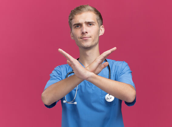 医生年轻的男医生穿着医生制服 手持听诊器 在粉红色的墙上显示出不被孤立的姿态年轻表演不愉快
