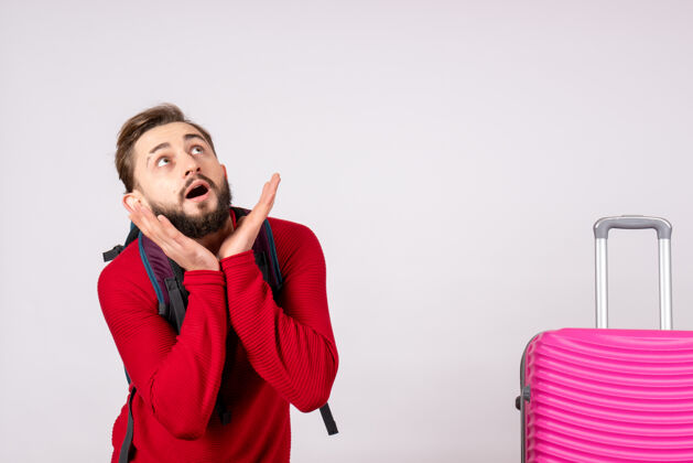 成人正面图：年轻男性游客带着背包和粉色包在白色墙壁上covid飞机度假情感病毒飞行色彩情绪游客飞行