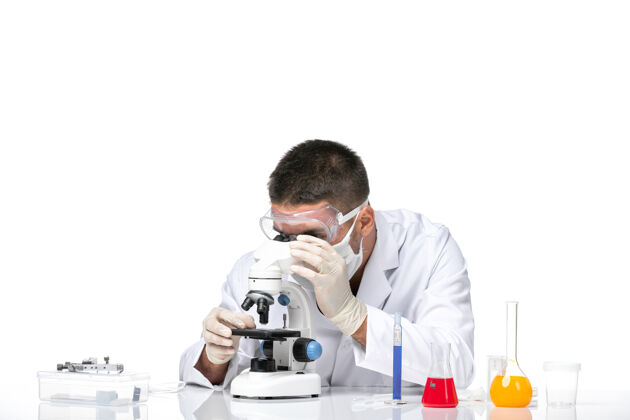 视图正面图：男医生穿着白色医疗服 戴着面罩 在白色办公桌上使用显微镜男性男性医生大流行