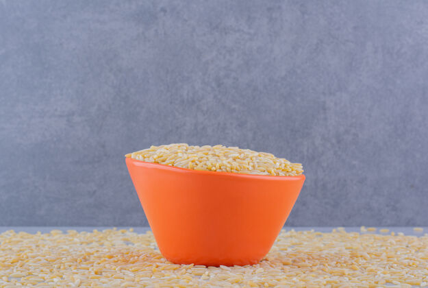 碳水化合物满满的饭碗坐在大理石表面散落的一团糙米上谷物饮食米饭