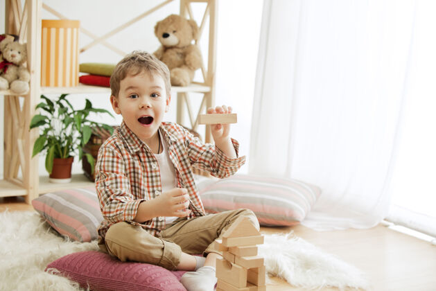 塔楼坐在地板上的小孩在家里玩木块的男孩面带微笑 惊讶不已概念图 带复制品或负片空间 还有你的文本模型学校玩具建造