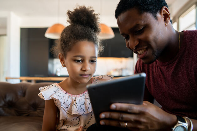 男人一个女儿和父亲在家里玩数字平板电脑的照片幼儿父母肖像