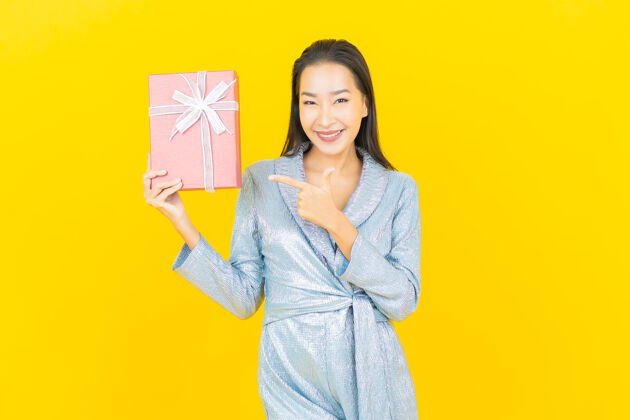 女人肖像美丽的亚洲年轻女子微笑与红色礼品盒在黄色的墙壁蓝色礼物礼物盒
