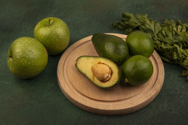 食物木制厨房板上有机鳄梨的俯视图 绿色背景上隔离着青苹果和欧芹的酸橙蔬菜苹果鳄梨
