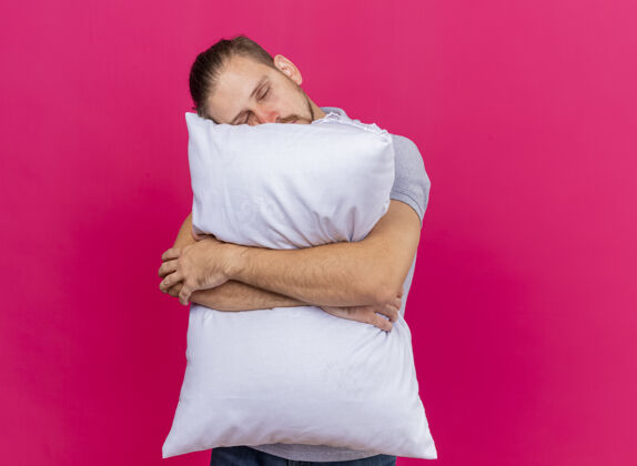 困倦昏昏欲睡的年轻英俊的斯拉夫病夫抱着枕头把头枕在上面闭着眼睛隔离在粉红色的墙上 留着复印空间衣服眼睛拥抱