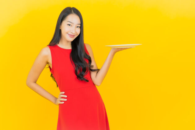 饮食画像美丽的亚洲年轻女子微笑着在黄色的墙上空盘子杯子肖像工作