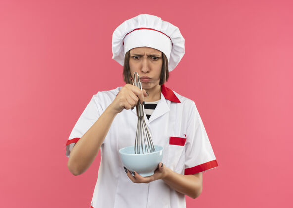 搅拌穿着厨师制服的年轻女厨师拿着面团和碗 看着粉红色背景上的复制空间厨师女年轻