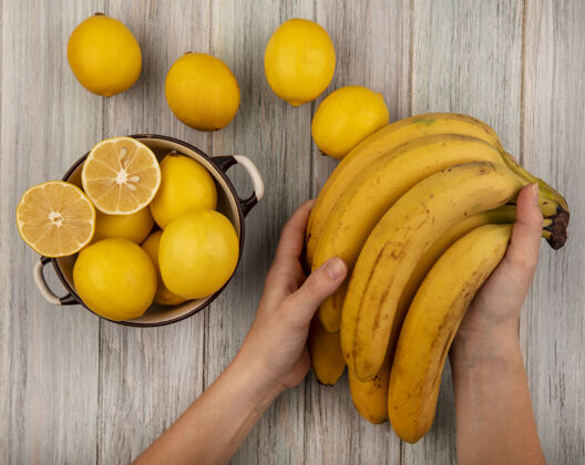 灰色女性手拿着香蕉和柠檬放在碗里的顶视图 柠檬被隔离在灰色的木制背景上木头女性视图