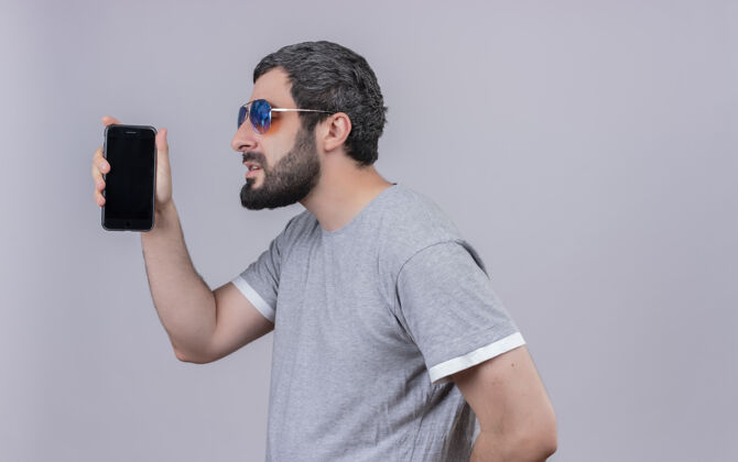 年轻年轻英俊的白种人戴着墨镜站在侧视图中 手持手机 背景为白色 留有复印空间手机站着手机