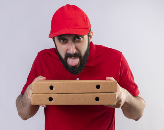 帽子年轻英俊的白人送货员 穿着红色制服 戴着帽子 手里拿着披萨盒 在白色背景上露出孤立的舌头盒子年轻舌头