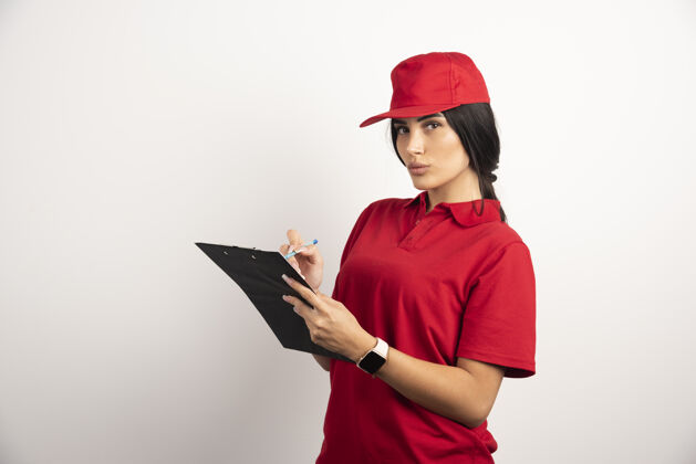 工人红色制服的快递员在剪贴板上写下订单高质量的照片黑发女孩送货员