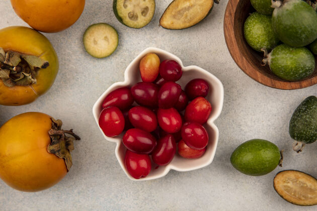 美味一碗美味的山茱萸樱桃的俯视图 灰底上孤立着飞珠和柿子灰色樱桃柿子