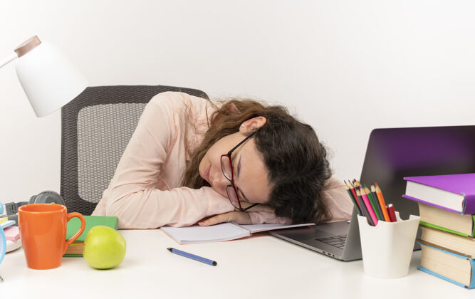 眼镜疲惫的年轻漂亮女学生戴着眼镜睡在书桌旁 白色背景上孤立着学习工具漂亮女学生学校