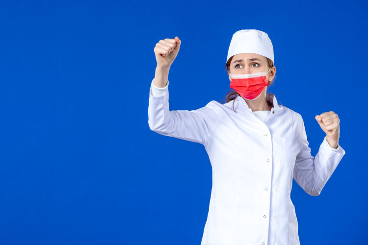 正面正面图身着医疗服的年轻护士 蓝色墙上戴着红色防护面具药套装成人
