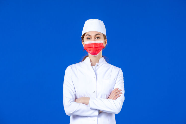 年轻护士正面图身着医疗服的年轻护士 蓝色墙上戴着红色防护面具面罩成人蓝色