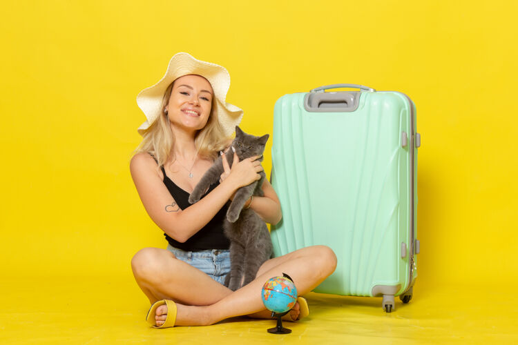 年轻正面图年轻的女性坐在她的绿色袋子抱着小猫在黄色的墙上旅行度假海上旅行太阳猫景色漂亮
