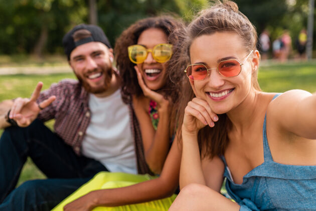 多种族五彩缤纷时尚快乐的年轻朋友陪伴坐在公园里 男女同乐太阳镜多样性女人