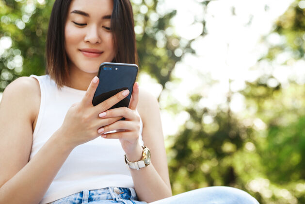 娱乐亚洲年轻女子坐在公园里用手机的特写镜头放松聊天Wifi