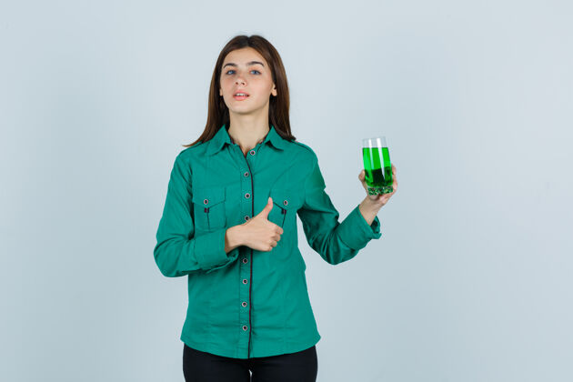 肖像年轻女孩拿着一杯绿色液体 穿着绿色上衣 黑色裤子 竖起大拇指 表情严肃正面图严肃愤怒模型