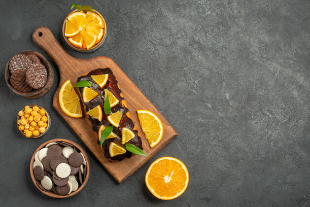 切割上图：美味的蛋糕切橘子和饼干放在深色桌子的砧板上美食黑暗盘子