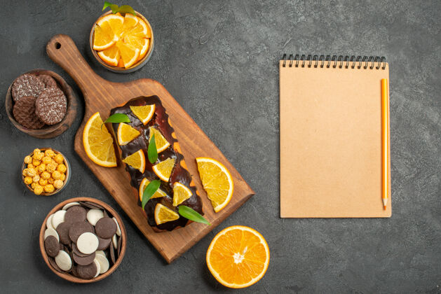 烹饪美味蛋糕的水平视图切橘子 饼干和笔记本放在深色桌子的砧板上盘子饼干深色