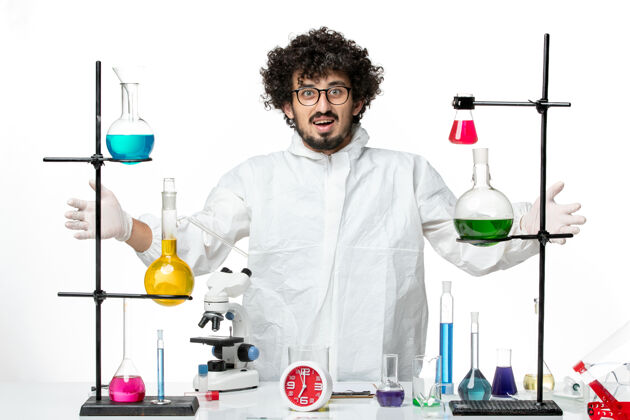 实验室正面图身着特殊套装的年轻男性科学家站在桌子周围 白色墙壁上有解决方案实验室化学烧杯