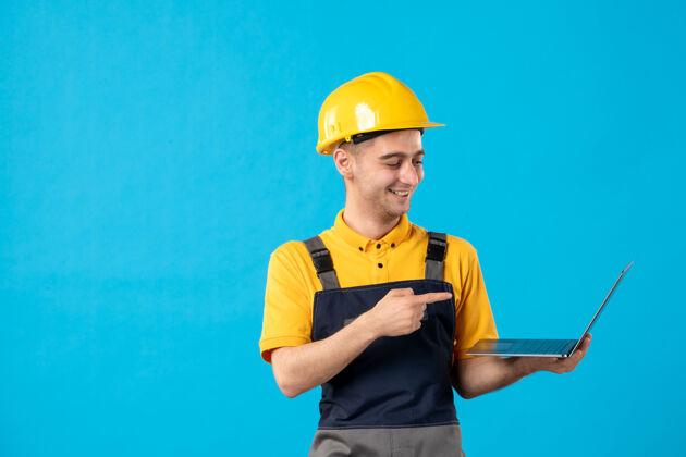 帽子蓝色表面上穿着制服 手持笔记本电脑的男性工作人员的正视图男人建筑商专业