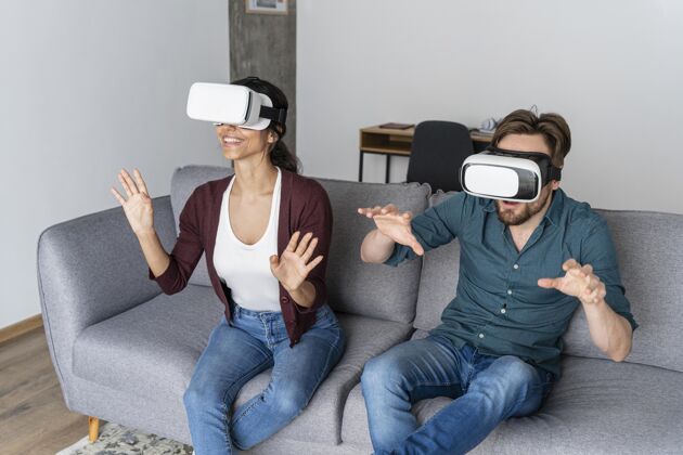 娱乐男人和女人在家里的沙发上与虚拟现实耳机虚拟现实乐趣房子
