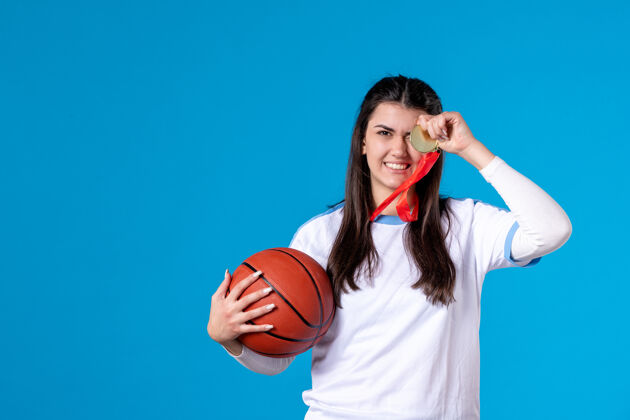 篮球正面图：年轻女子拿着篮球站在蓝色的墙上蓝举行年轻女性