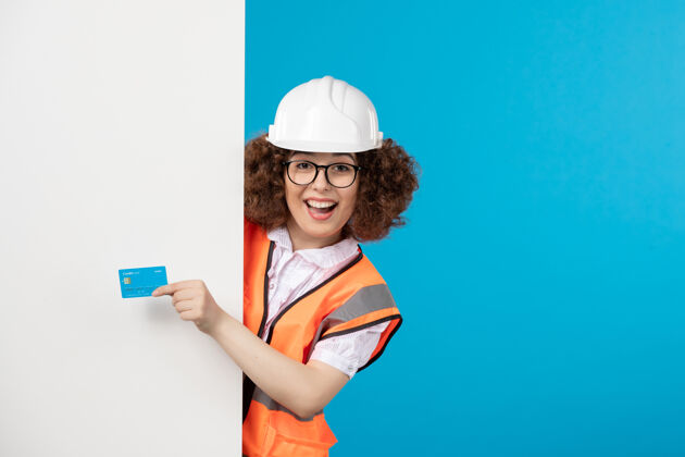 工人穿着制服的女建筑工人的正视图 蓝色的墙上有蓝色的银行卡制服蓝色人