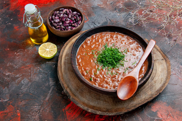 勺子经典的番茄汤在一个棕色的碗里 油瓶豆子和勺子放在五颜六色的桌子上油胡椒蔬菜