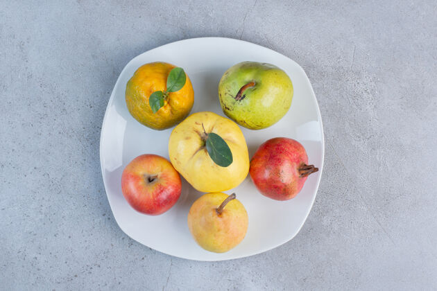 天然把石榴 梨 橘子 木瓜和苹果放在大理石背景的盘子里风味美味石榴