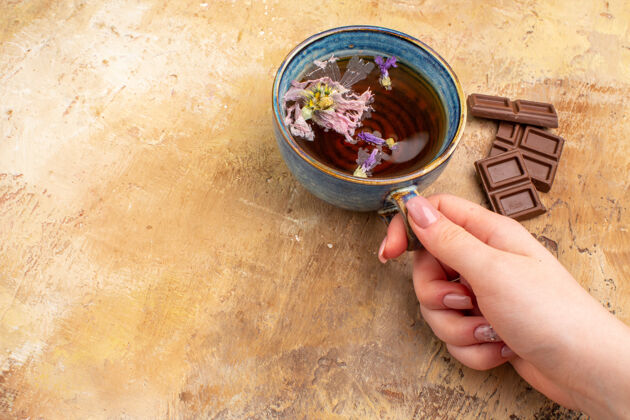 巧克力手拿一杯热花草茶和巧克力放在五颜六色的桌子上凉茶食物汤碗