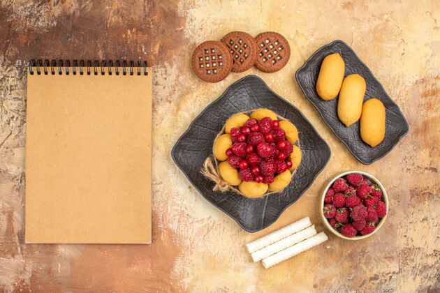 饮食一个礼物蛋糕和饼干放在棕色盘子上水果和笔记本放在五颜六色的桌子上盘子食品胡椒粉