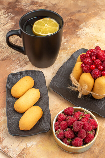水果一个礼品蛋糕和茶放在一个黑杯子里 柠檬和饼干放在五颜六色的桌子上草莓食品盘子