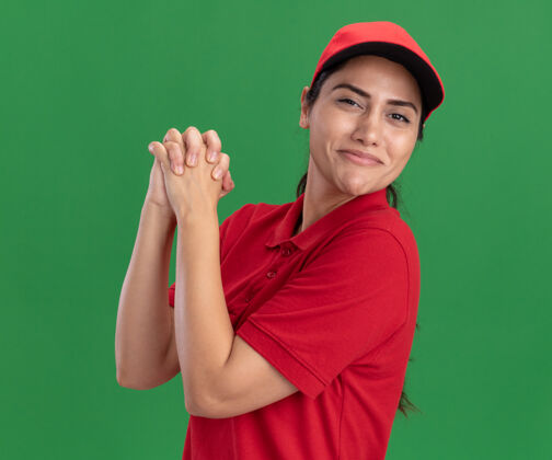 制服身着制服 头戴礼帽 在绿色墙壁上展示握手手势的年轻送货女孩很高兴表演送货请
