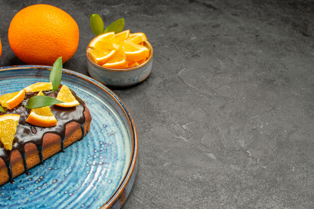 柑橘托盘上放着半张松软可口的蛋糕 黑桌子上放着橙子柑橘新鲜美味蛋糕