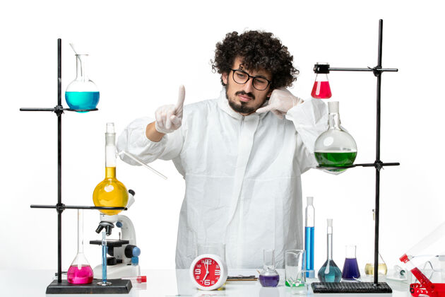 研究正面图身穿白色特殊套装的年轻男性科学家站在桌子旁 拿着解决方案化学套装烧杯