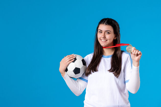 比赛前视图：年轻女子在蓝色墙上拿着足球青少年奖牌比赛