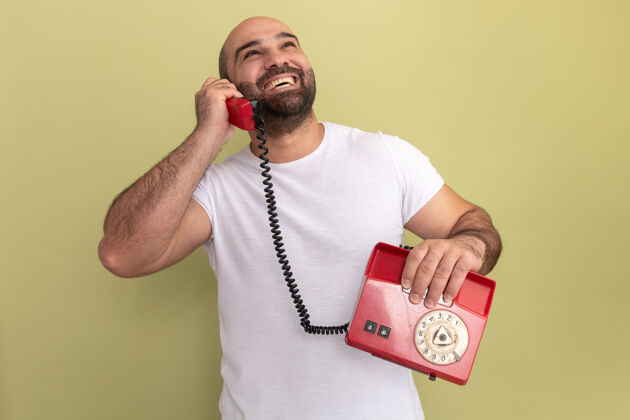男人一个留着胡子的男人穿着白t恤 站在绿色的墙边 对着一部旧电话微笑着胡子站着老人