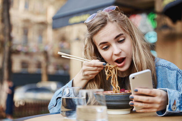 微笑可爱的女孩吃着中国面条看着手机 手里拿着c年轻手机中国人