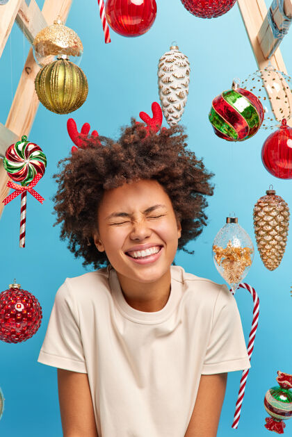乐观快乐和喜庆的事件概念快乐快乐的黑皮肤女人笑出来闭上眼睛 微笑着去装饰圣诞树穿着休闲白色t恤享受寒假庆祝欣喜若狂种族