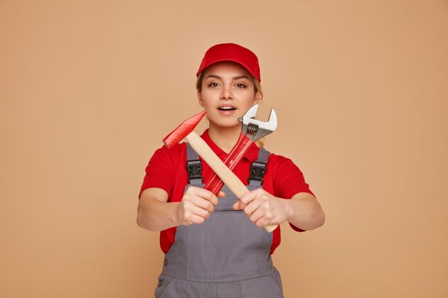 年轻兴奋的年轻女建筑工人戴着帽子和制服 伸出扳手和锤子对着镜头 没有做任何动作制服兴奋手势