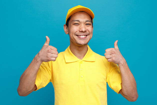 拇指快乐的年轻送货员穿着制服 戴着帽子 竖起大拇指年轻交货制服